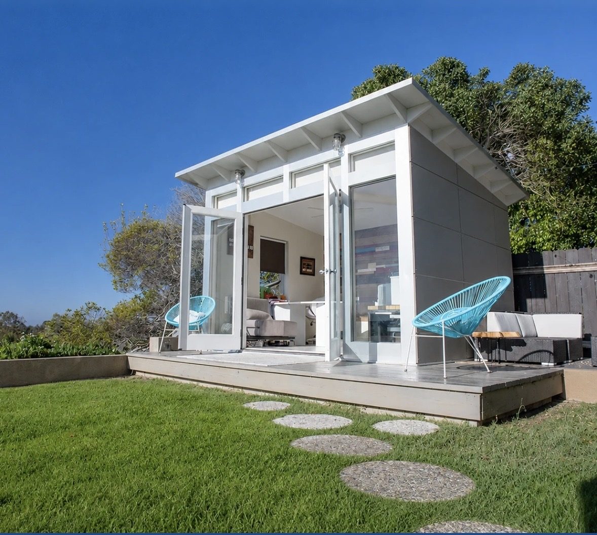 Backyard studio exterior with white cladding, bifold doors, and outdoor lounge seating